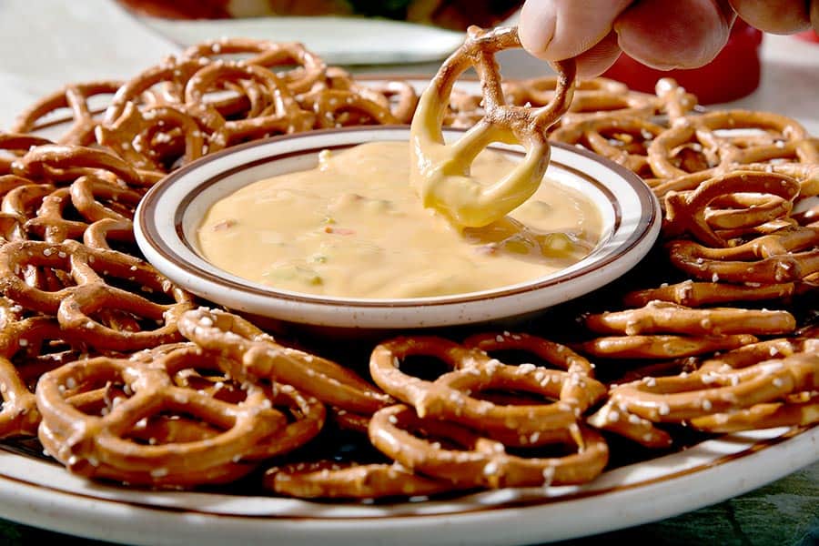 Plate of pretzels and a man dipping a pretzel a bowl of cheese sauce