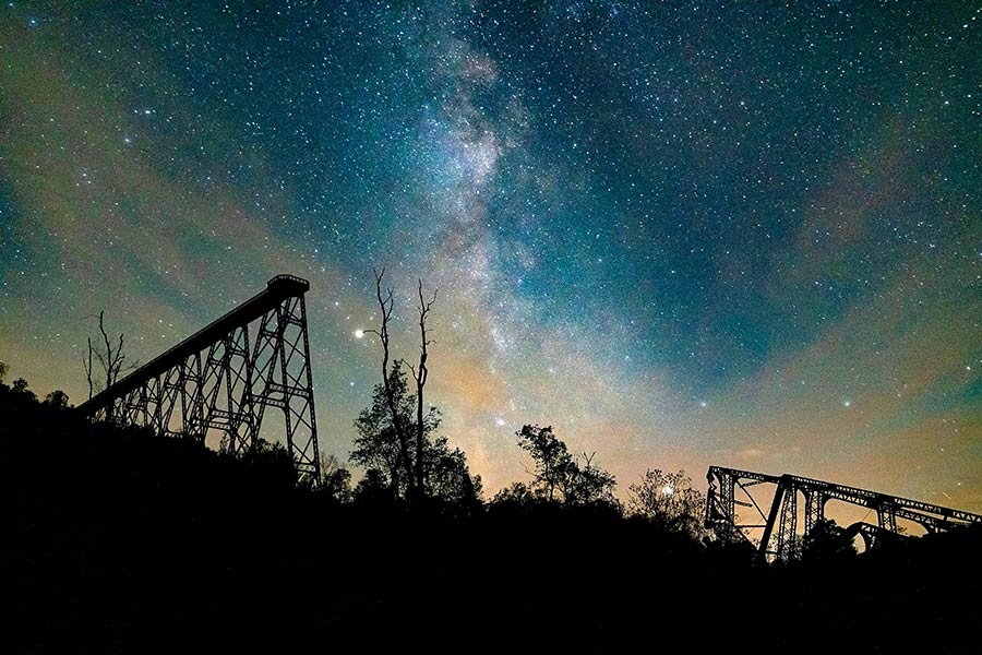 Milky Way Galaxy overhead with dark silhouette of mountain and bridge 