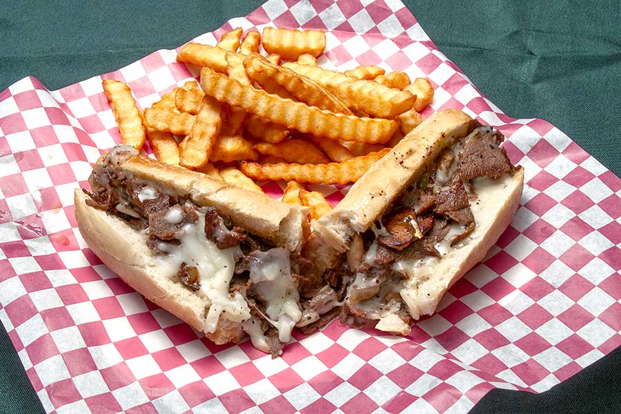 Cheesesteak sandwich with French fries on red and white checkered paper