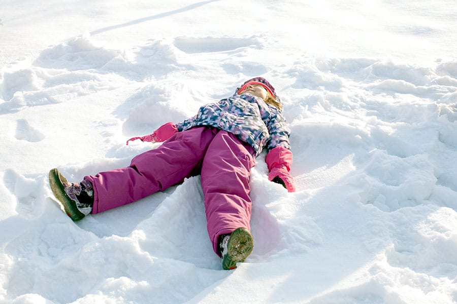 Girl in snow suit laying on her back making a snow angel in the snow