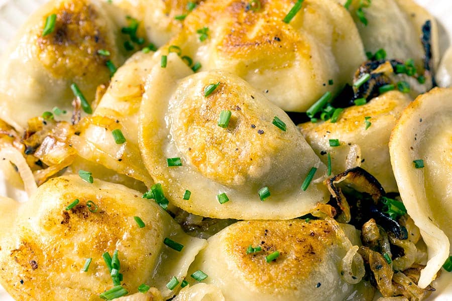 Dish of potato pierogies topped with onions and chive