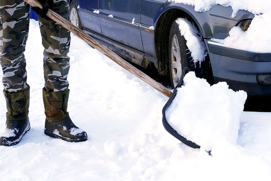 Man shoveling snow away from blue car