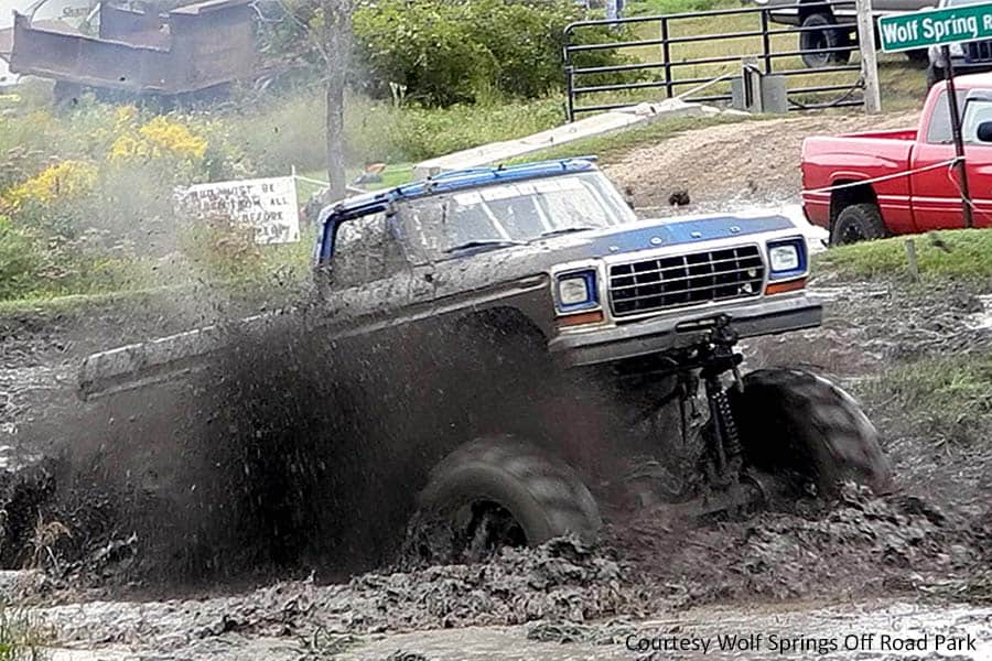 Blue Ford truck with large tires plowing through mud hole